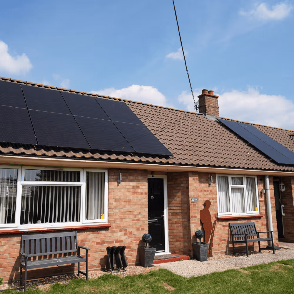 The front exterior of a brick bungalow at Mill View Bungalows, featuring a brown tiled roof with two large arrays of newly installed black solar panels and a decorative silhouette of a soldier.