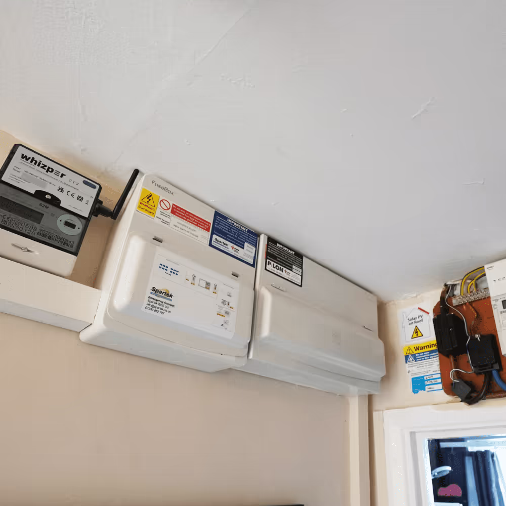 Interior shot of a newly installed consumer unit (fusebox), electricity meter, and solar PV connection box mounted near the ceiling, demonstrating the electrical components of a solar panel system installation.
