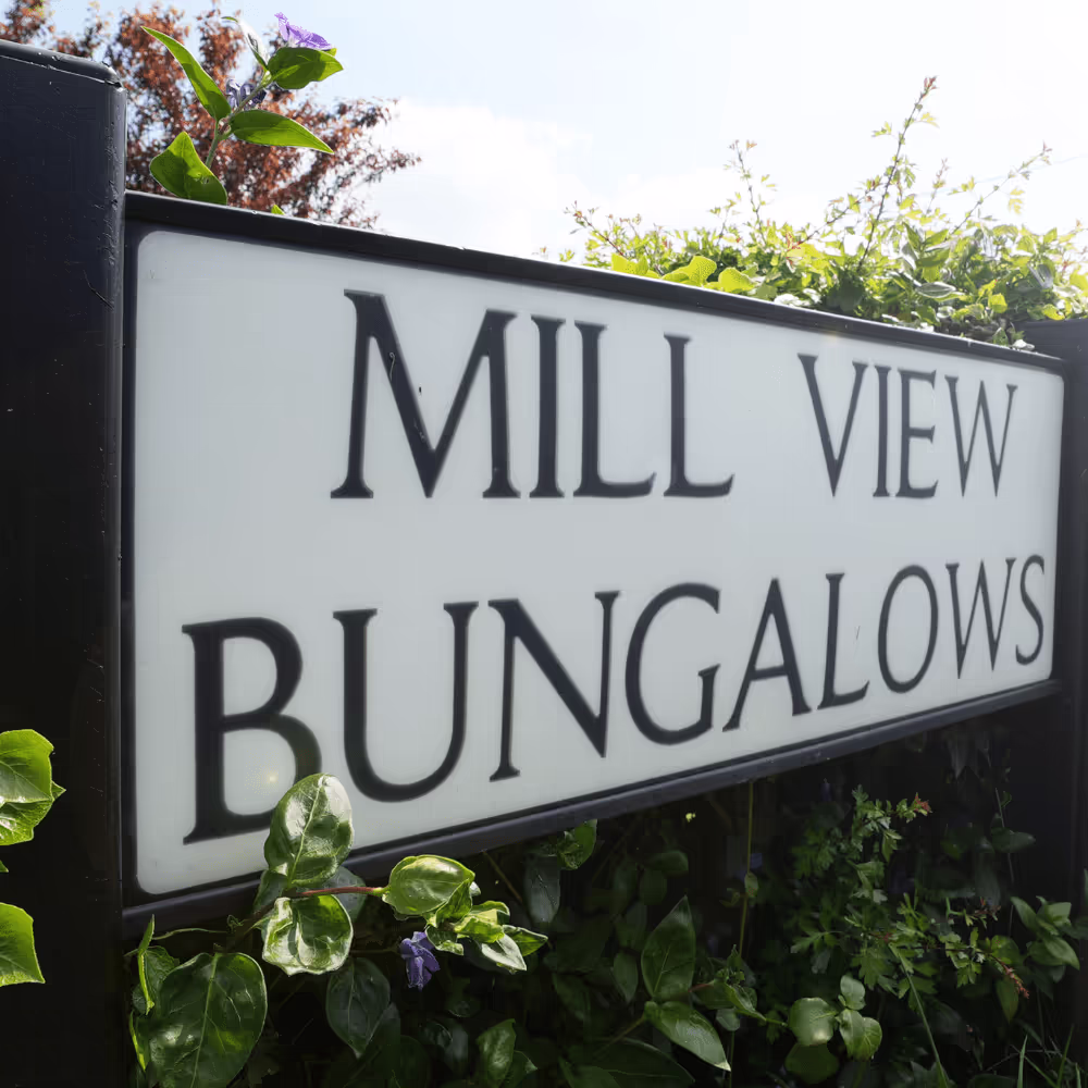A close-up of the illuminated street sign reading 'MILL VIEW BUNGALOWS', confirming the location of the solar installation project for Eastlight Community Homes.