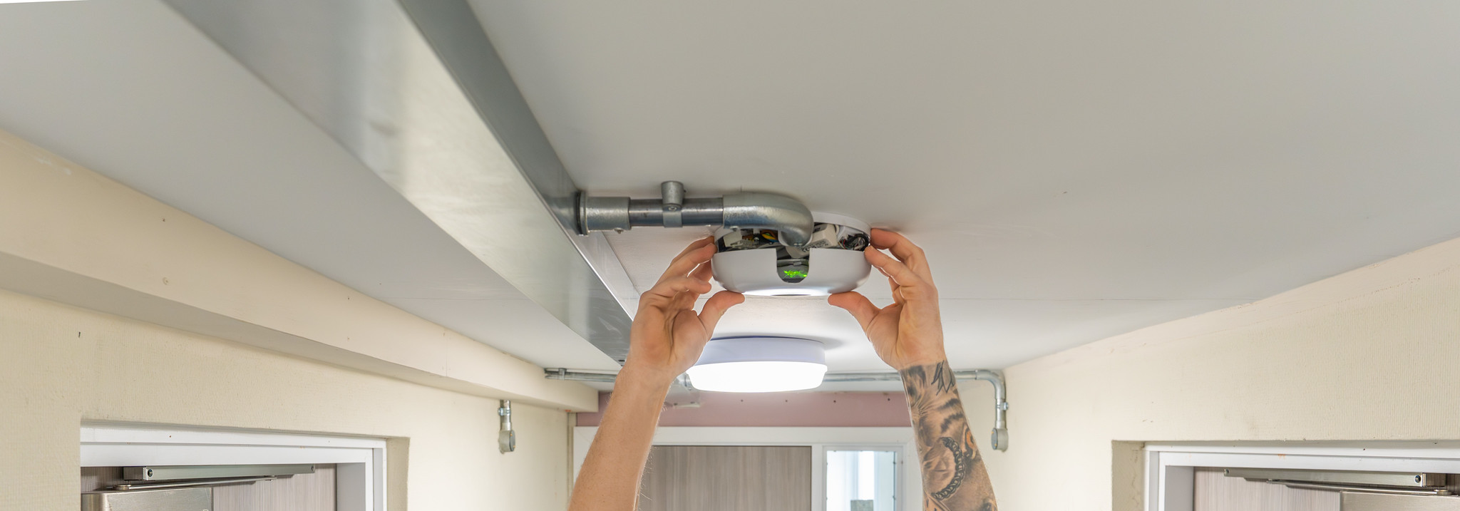 operative installing fire alarm onto ceiling of residential property corridor