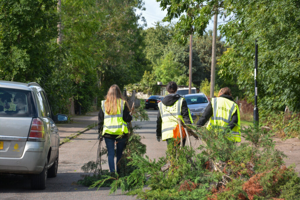 Team members wearing high visibility vests clearing branches from a residential street, supporting sustainable community initiatives.